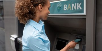 Portrait of an African American woman withdrawing money at an ATM and looking happy - financial concepts. **DESIGN ON BANK AND CREDIT CARD WERE MADE FROM SCRATCH BY US**